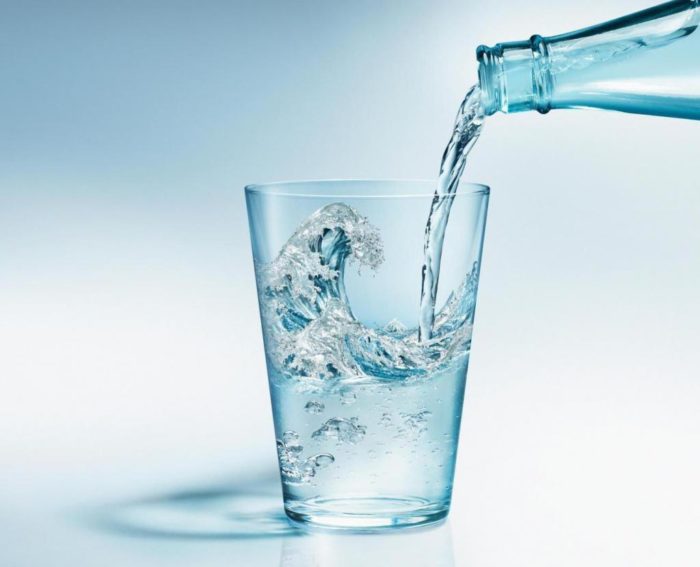 в стакан наливается минеральная вода из бутылки для человека, страдающего подагрой